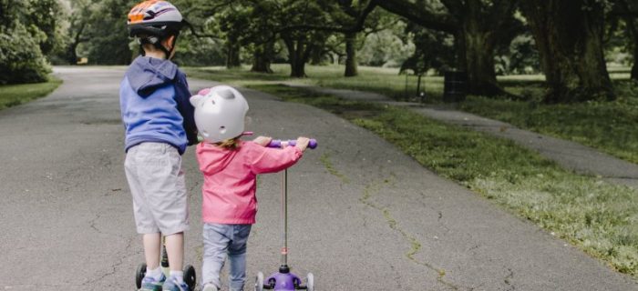 Zwei Kinder fahren mit einem Kinderroller