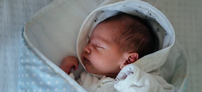 Ein Baby schläft in einem blauen Fußsack mit weißen Pünktchen