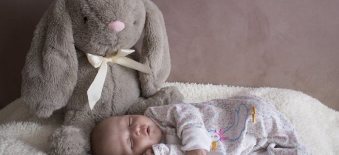 Ein schlafendes Baby in seinem Strampelanzug mit einem grauen großen Stoffhasen